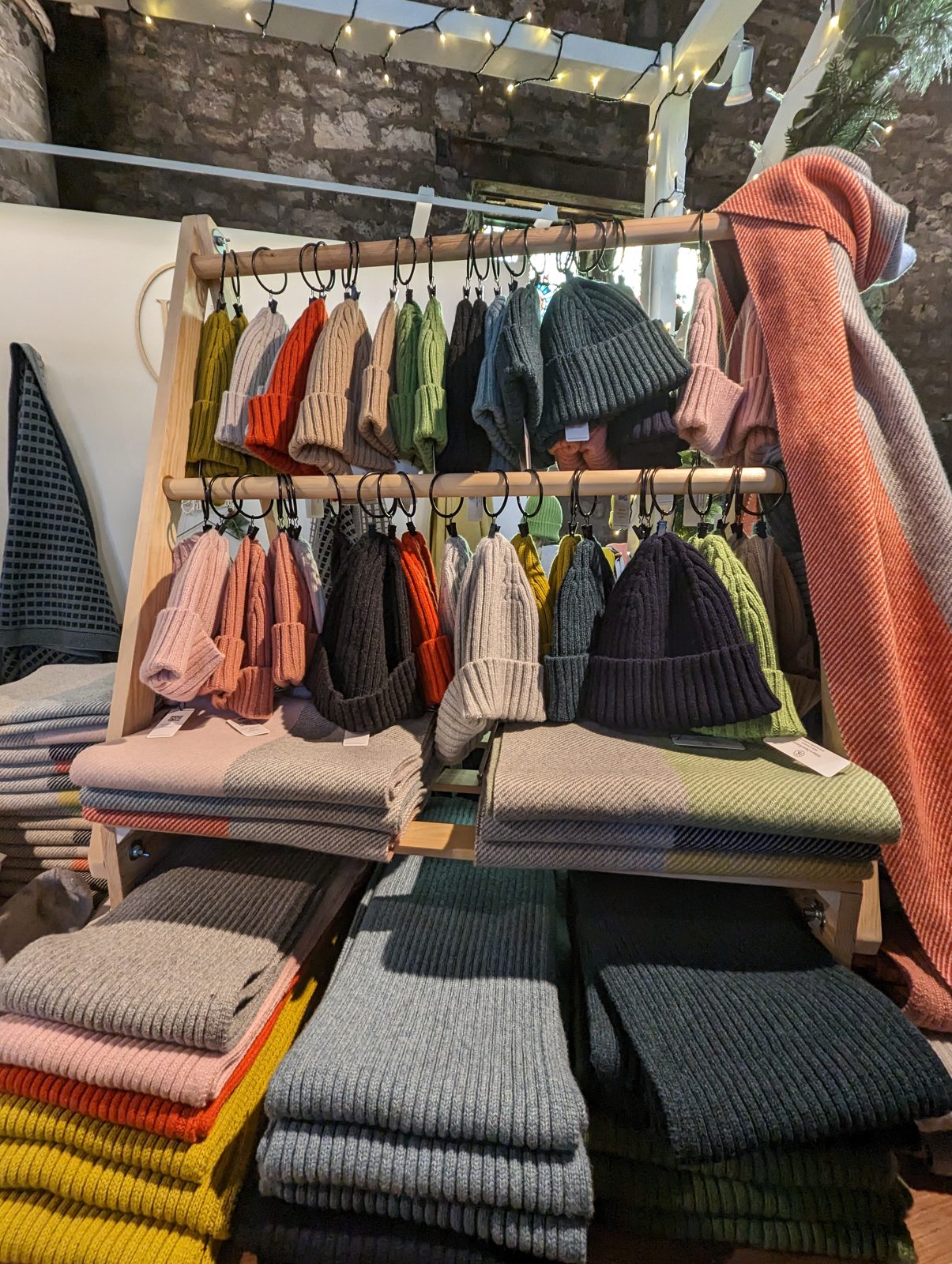 Rail of Scottish ribbed wool beanies above stacks of folded lambswool scarves in an Edinburgh Old Town shop.