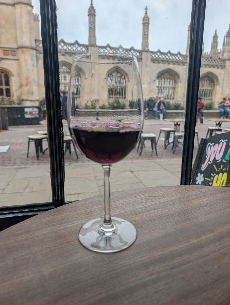 A glass of red mystery wine in the window of Cambridge Wine Merchants, with King's College across the street
