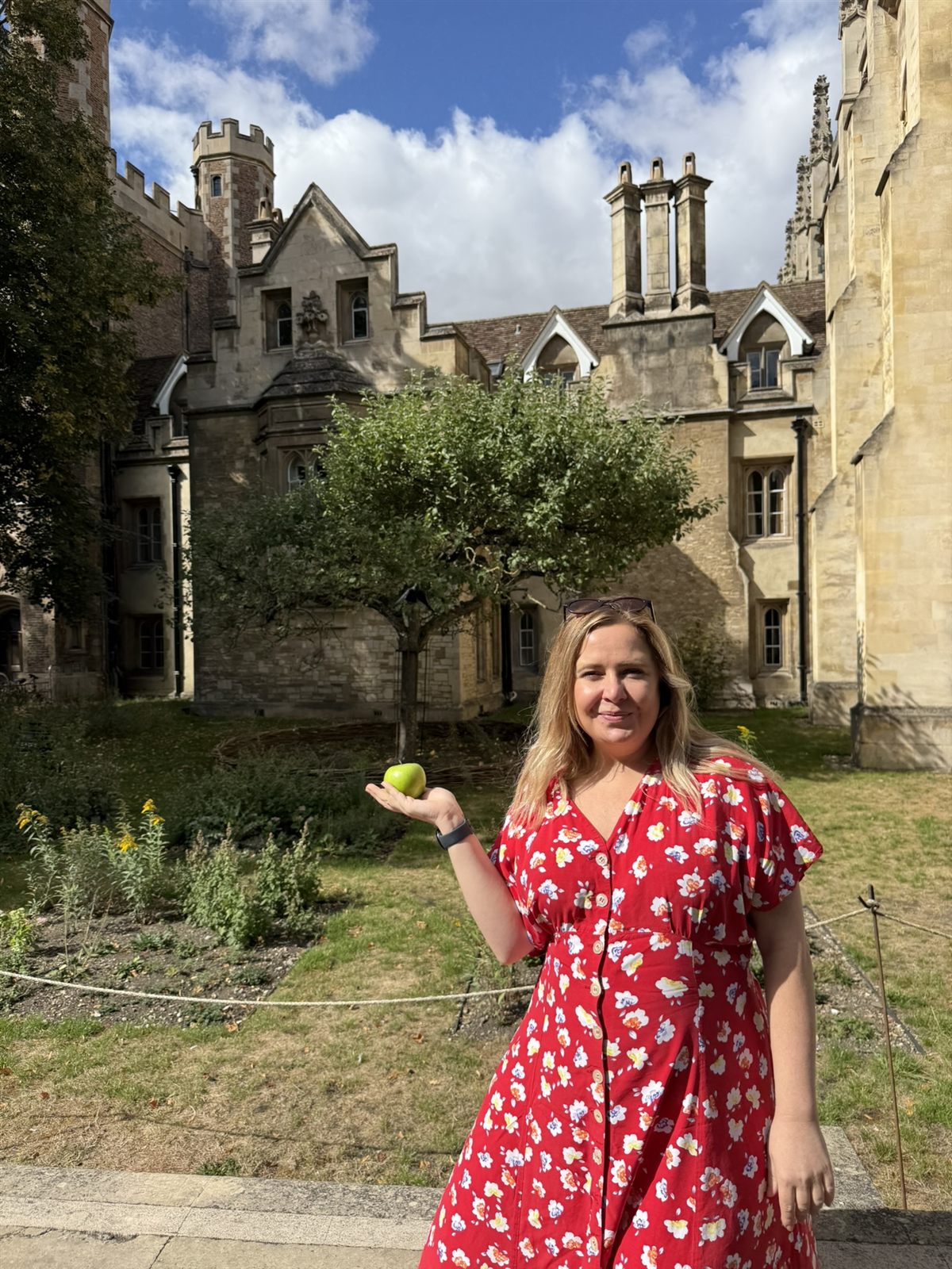 Kat holding a green apple in front of the grafted Newton apple tree at Trinity College, Cambridge