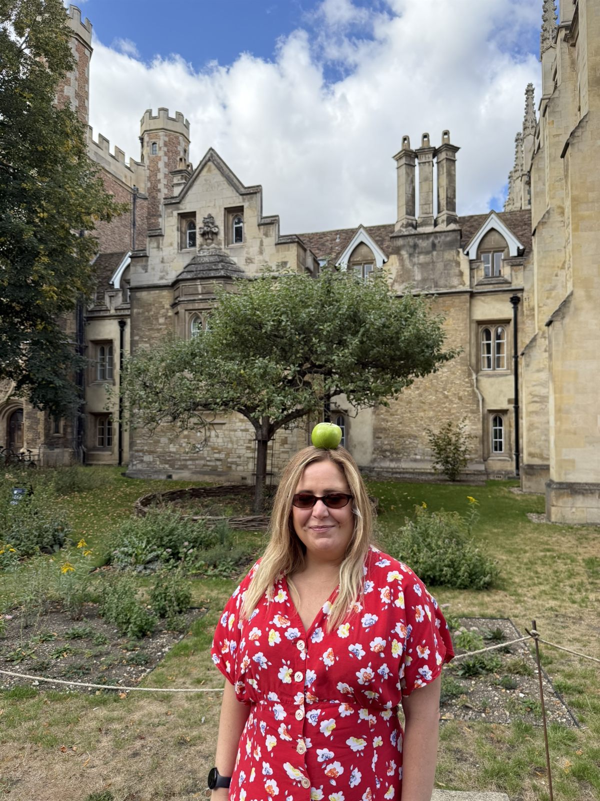 Kat balancing a green apple on her head in front of Newton's apple tree at Trinity College, Cambridge