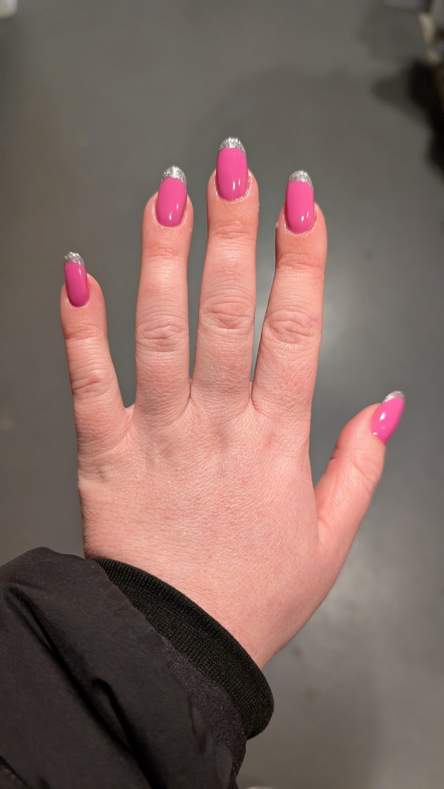 A hand with pink nails finished with silver glitter tips