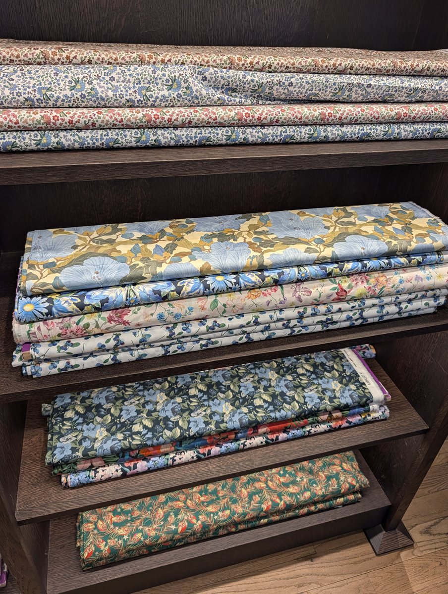 Folded floral cotton fabrics stacked on shelves at Liberty